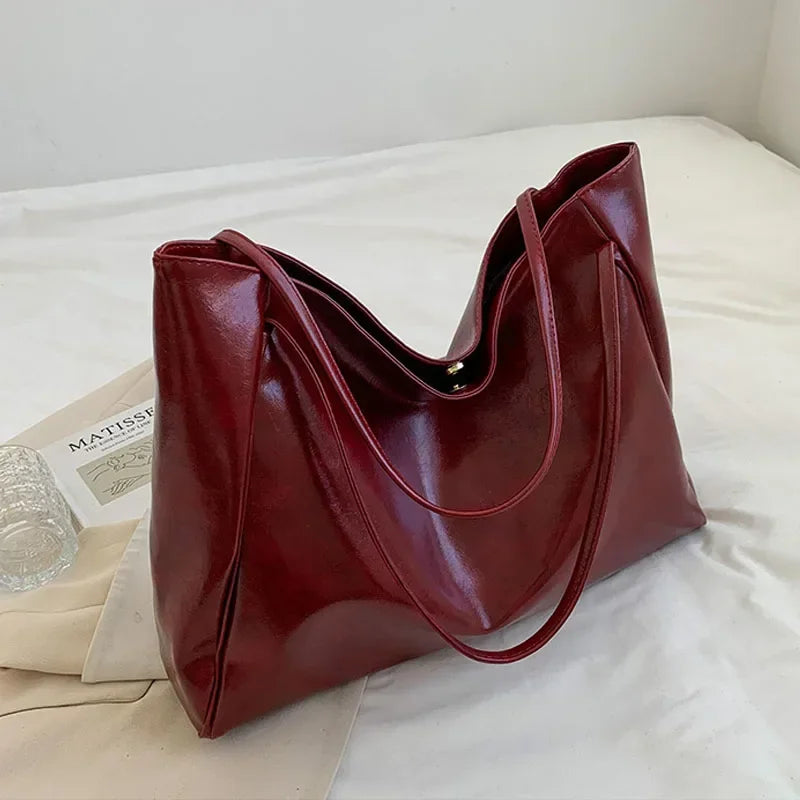 Sac seau aspect cuir souple bordeaux posé sur un lit