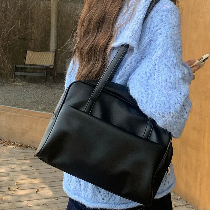 Sac à main aspect cuir noir porté à l'épaule
