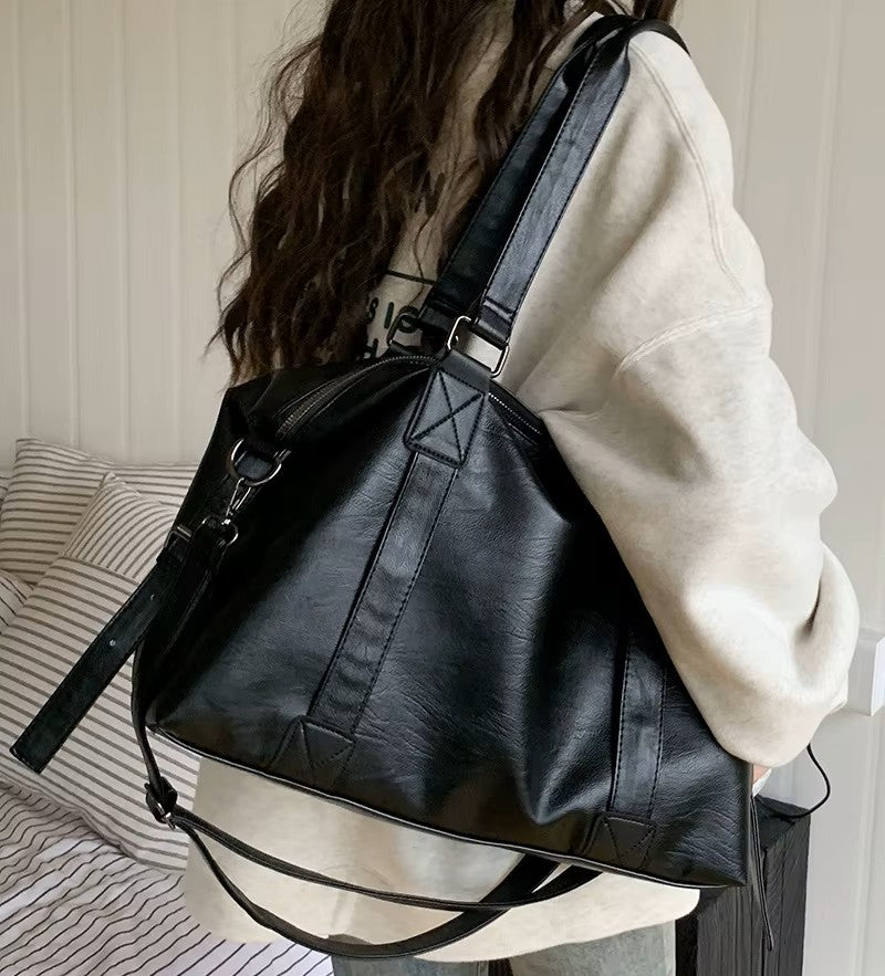 Sac fourre-tout aspect cuir noir porté à l'épaule, vue de dos