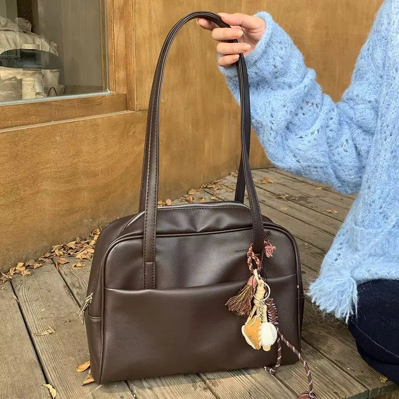 Sac à main aspect cuir marron tenu par les anses
