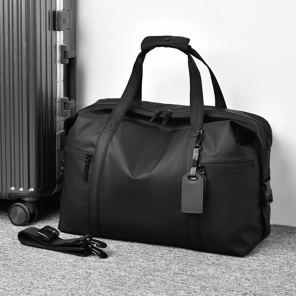 Sac de voyage homme noir posé au sol à côté d'une valise